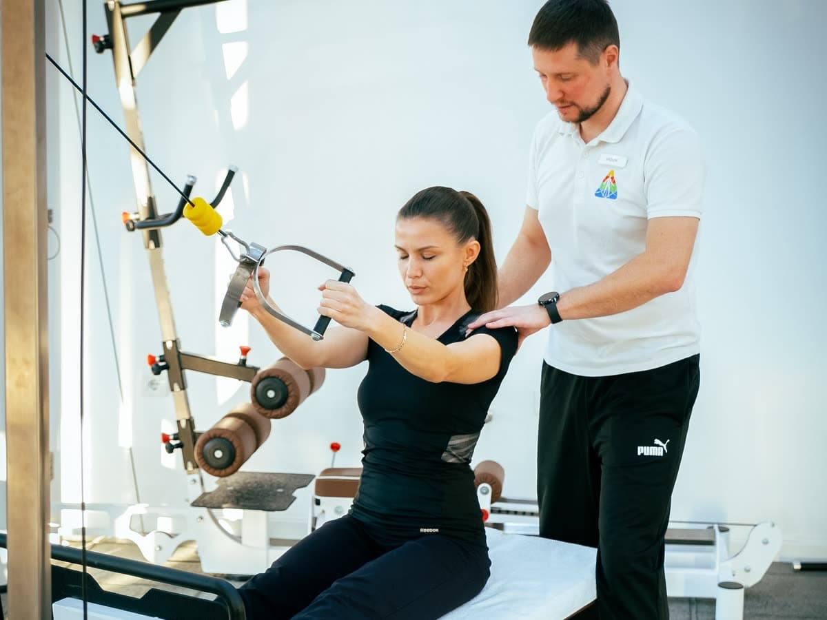 A patient working rehabilitation equipment with a therapist standing alongside