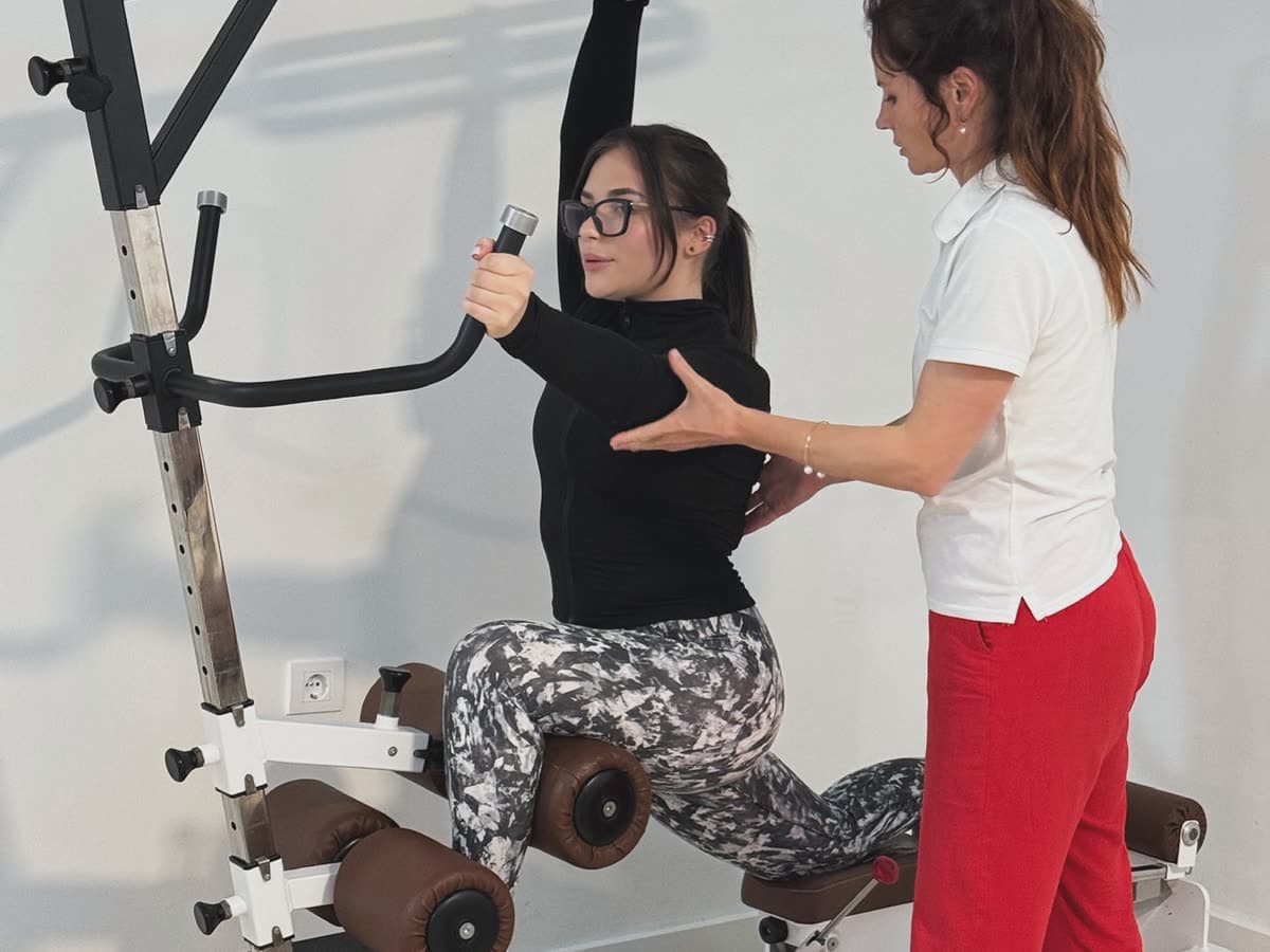 A patient working an overhead pull with a therapist alongside
